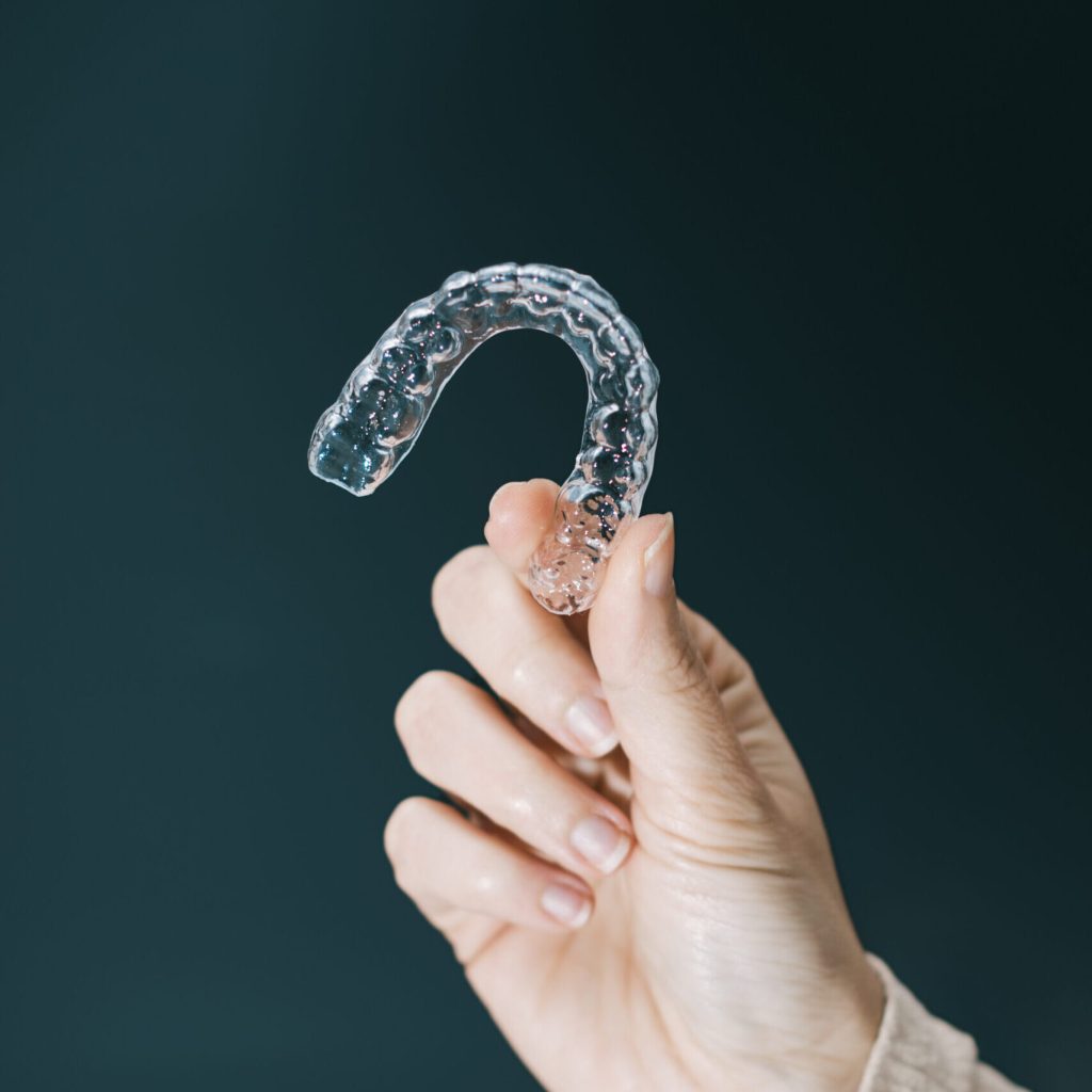 woman's hand holding a side lit transparent retainer on dark green background